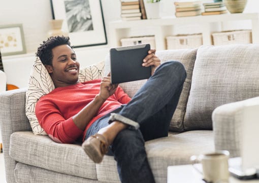 Wiley Insurance Services | Rock Hill, SC | Man laying on couch in his condo smiling and looking at a tablet relaxing